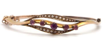 A 9ct pink stone and seed pearl bangle, the centre leaf shape frame set with five graduated round