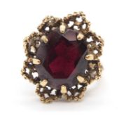 A 9ct garnet ring, the claw mounted oval garnet set within a textured scalloped outer frame, with