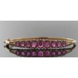 A Victorian style 9ct ruby and diamond hinged bangle, the upper half set with nine graudated oval