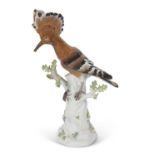 A Meissen model of a Hoopoe bird on a tree trunk, the trunk decorated with insects and flowers, blue