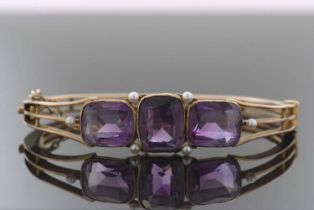 A late 19th century amethyst and seed pearl bangle, set with three rectangular amethysts in collet