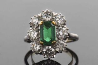 An emerald and diamond cluster ring, the central claw mounted emerald cut emerald, approx. 8.4 x 5.5