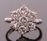A diamond flowerhead cluster ring, the central round brilliant cut diamond, surrounded by 6 round