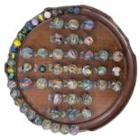 A vintage wooden solitaire board, with a collection of glass marbles. Significant damage to edges of
