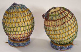 Two Orstrich eggs in traditional Kenyan massai beeded netting set on padded plinths