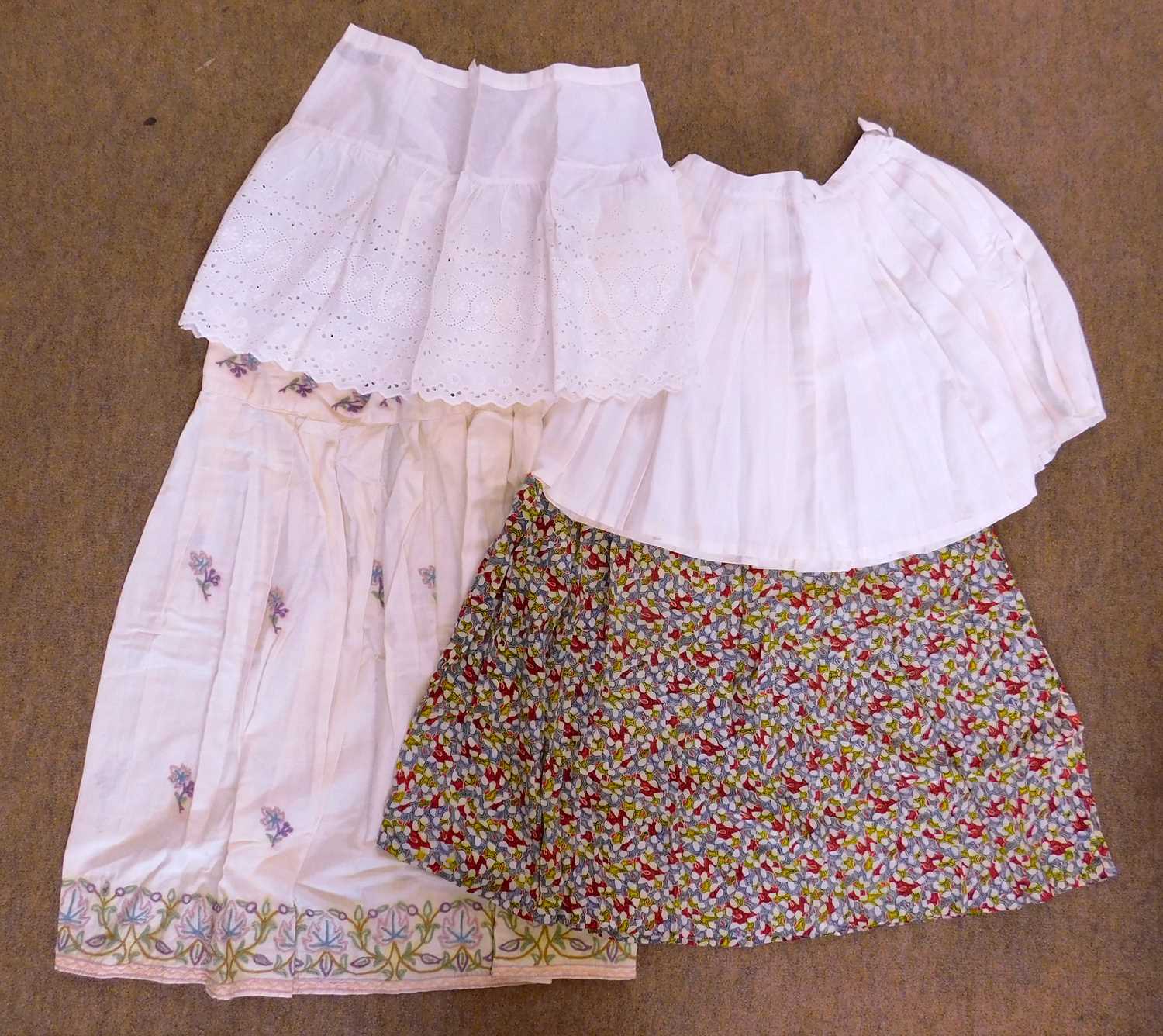 Four mid-20th century skirts, to include a floral patterned skirt, a cream cotton skirt with