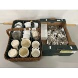 Wicker basket containing various royalty commemorative mugs, a box of silver plated cutlery and