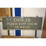 A metal sign "Danger Please Keep Clear of Walls"