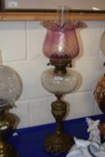 A brass based oil lamp with clear font and pink tinted frilled shade