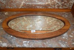 An oval bevelled wall mirror in oak frame
