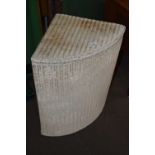 A corner Lloyd Loom style laundry basket