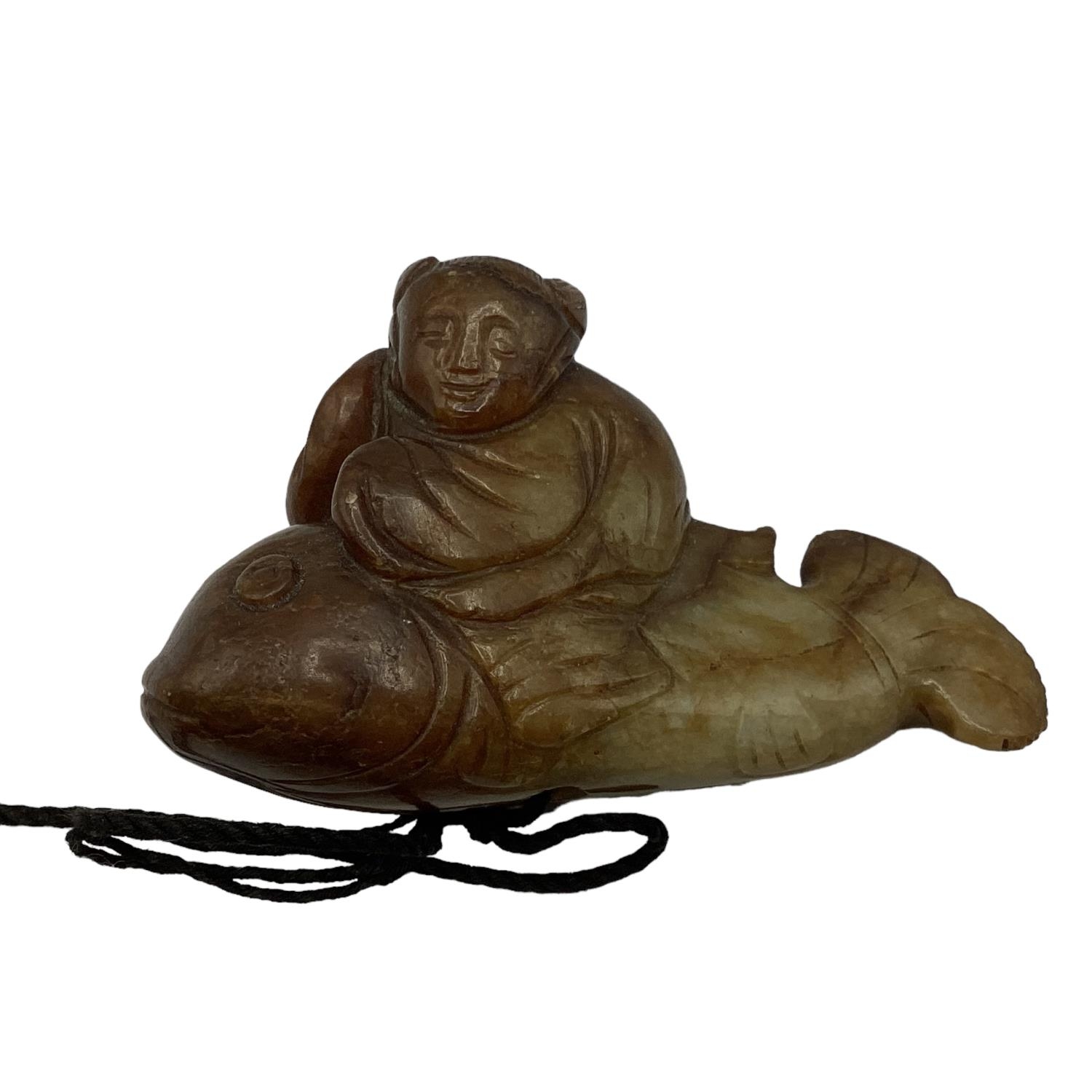 A carved jade figure of a man riding a fish 7cm x 4cm.