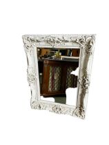 A decorative rectangular wall mirror, with white scrolling ornate frame