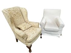 Two cream upholstered arm chairs, one traditional winged arm chair, the other a smaller modern