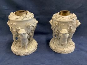A pair of Moore Bros, cherub stands, 24cm H, some losses