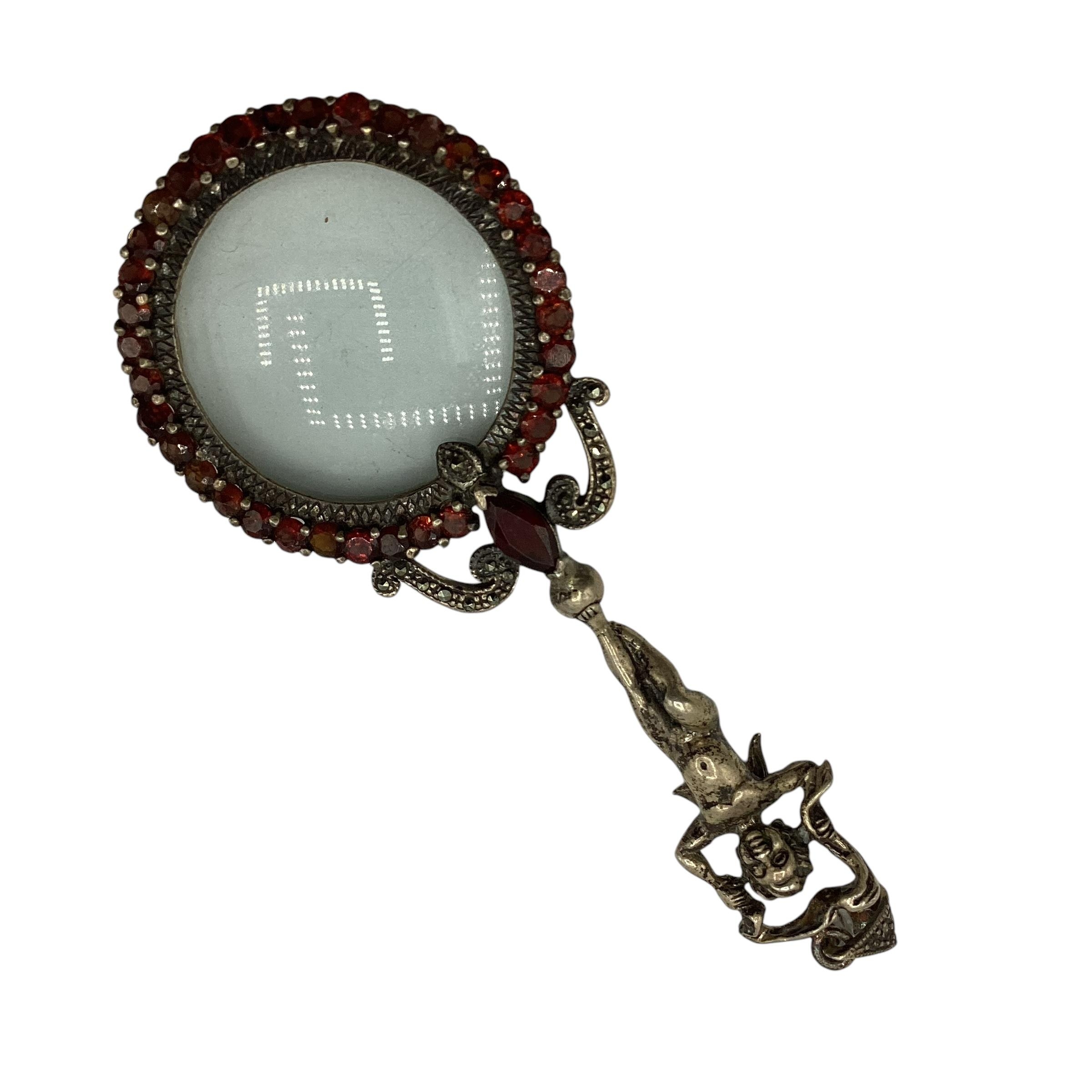 A 924 silver magnifying glass with cast putti handle and red garnet surround.