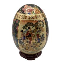 An Oriental ceramic egg with Satsuma style gilt and floral decoration on hard wood stand. 22cm(h).