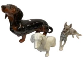 Three china dogs to include a Beswick Dachsund, A German Shepherd, Nymphenburg seated dog