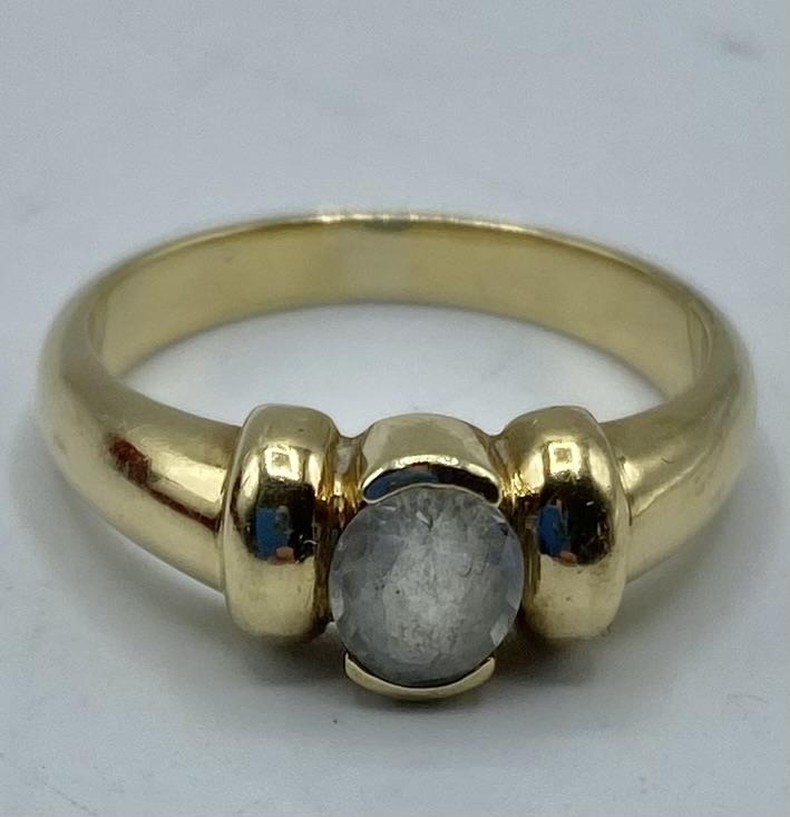 A 14ct gold and white sapphire single stone ring, central oval free cut bezel set sapphire. 4.46g.