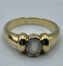 A 14ct gold and white sapphire single stone ring, central oval free cut bezel set sapphire. 4.46g.