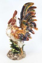 A large glazed pottery model of a cockerel, shown standing on a naturalistic base, h.58cm (a/f)