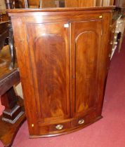 An early Victorian mahogany bowfront double door hanging corner cupboard, having twin short lower