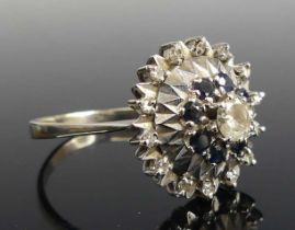 A white metal, sapphire and diamond reverse cluster ring, featuring a centre round brilliant cut