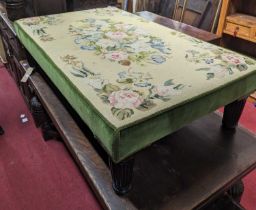 An oversized floral needlework upholstered footstool, raised on turned and reeded slightly