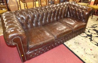 A chocolate brown leather buttoned upholstered three-seater Chesterfield, having three removable