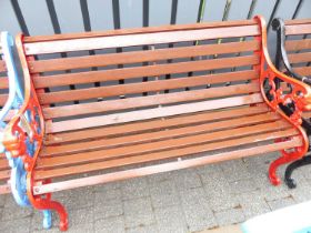 A red painted pierced and cast iron ended and stained slatted wood two-seater garden bench, width