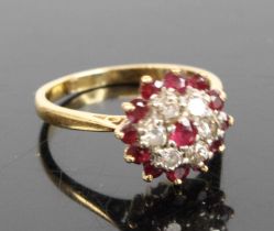 An 18ct gold ruby and diamond circular cluster ring, featuring a centre round ruby within a border