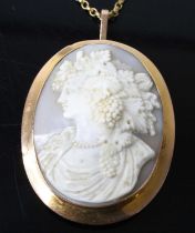 A yellow metal oval shell cameo brooch, depicting a classical woman within a bezel setting, with
