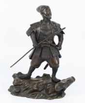 A Japanese bronze okimono of a warrior standing on a rocky outcrop with spear, 20th century, h.34.