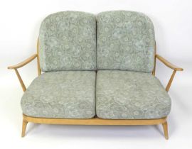 An Ercol blond beech stickback two-seater Windsor sofa, having slightly pronounced arm rests, webbed