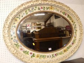 A decorative floral and cream painted oval bevelled wall mirror, having moulded repeating leaf