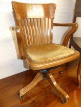 A 1930s oak tub slat back swivel desk elbow chair, raised on roller castors, width 57cm Supports