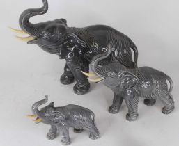 A graduated set of three pottery elephants, each modelled standing with trunk raised, the largest