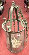 A patinated metal glazed hall lantern, of cylindrical shape, suspended from a chain, h.62cm (