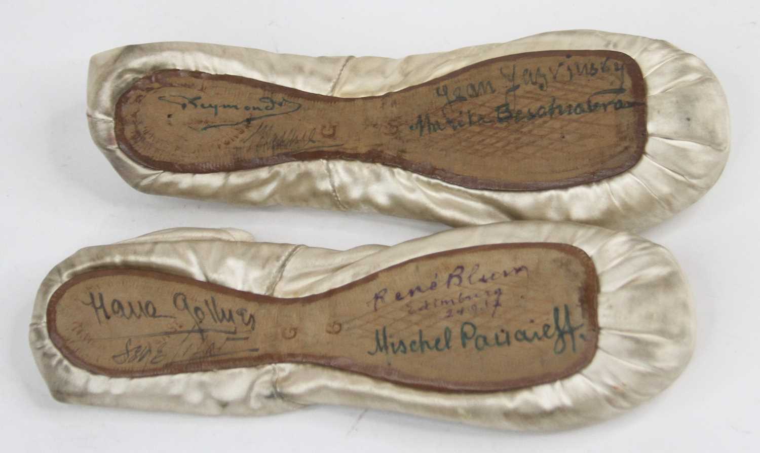A pair of vintage silk children's ballet pump shoes, each bearing signatures to the sole