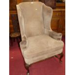 An early 20th century walnut framed and hide upholstered wingback armchair, having a squab cushion