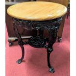A black painted cast iron based and beech topped circular pub table, the legs stylise decorated in