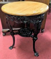 A black painted cast iron based and beech topped circular pub table, the legs stylise decorated in