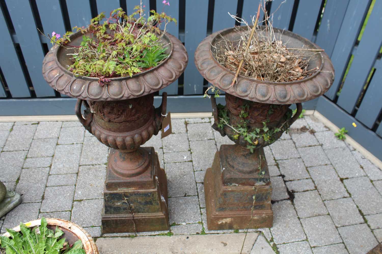 A pair of cast iron twin handled pedestal garden urns, raised on stepped tapering square bases,