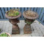 A pair of cast iron twin handled pedestal garden urns, raised on stepped tapering square bases,