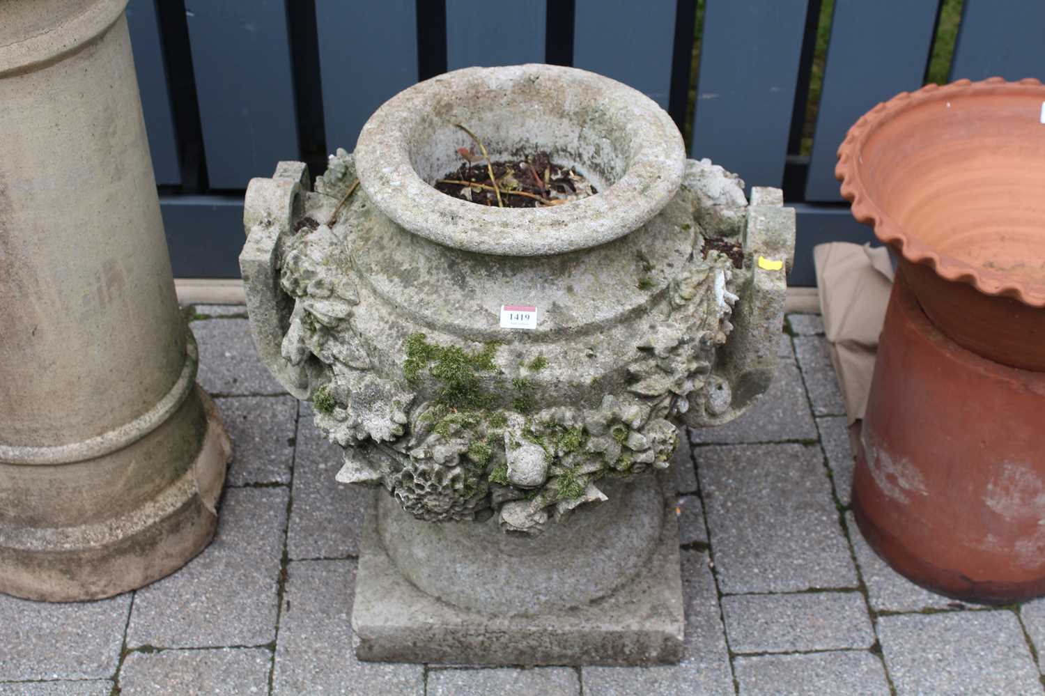 A reconstituted stone twin handled footed garden planter, decorated with heavy floral motifs, height