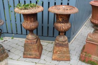 A pair of cast iron pedestal garden urns, each of reeded lower bulbous form and raised on square