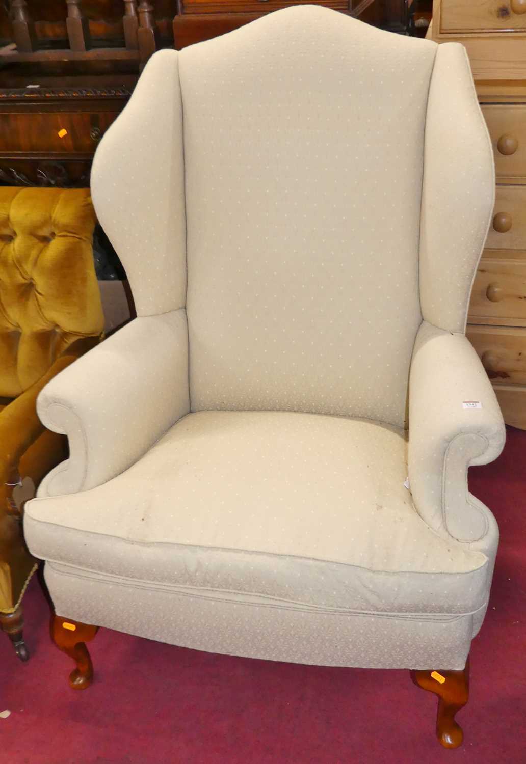 A contemporary cream floral fabric upholstered wingback scroll armchair, having squab cushion and
