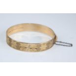 A 9ct gold hinged bangle, having bright cut engraved decoration, with gilt metal safety chain,