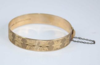 A 9ct gold hinged bangle, having bright cut engraved decoration, with gilt metal safety chain,