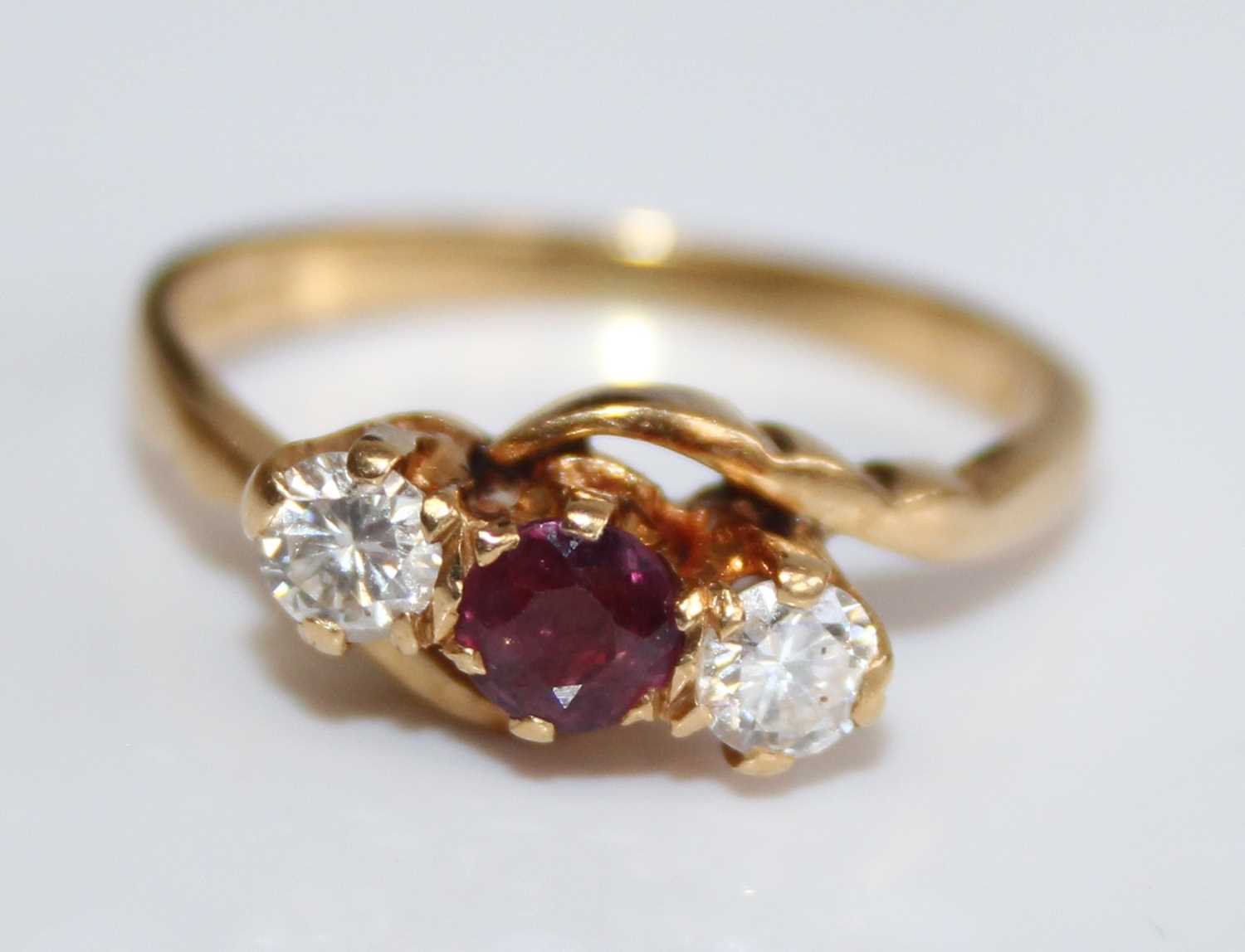 An 18ct gold, ruby and diamond three-stone crossover ring, the round cut ruby weighing approx 0.2